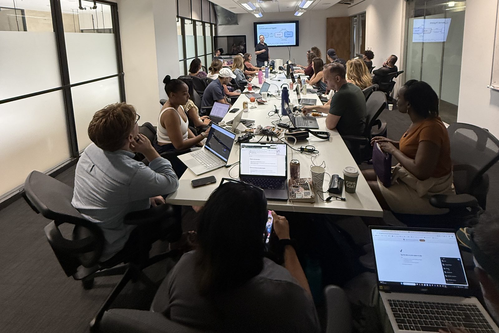 A workshop in Austin, seen from the back of the room: people along a long table working on their own laptops while Jonathan Malkin teaches at the screen.